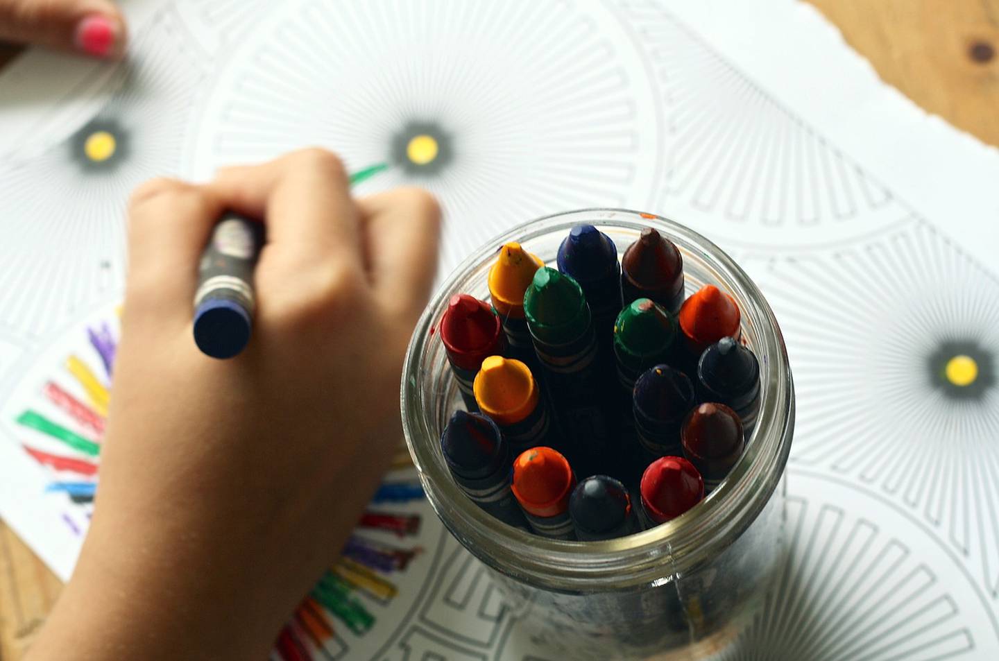 Mano de un niño pintando un dibujo con crayones.