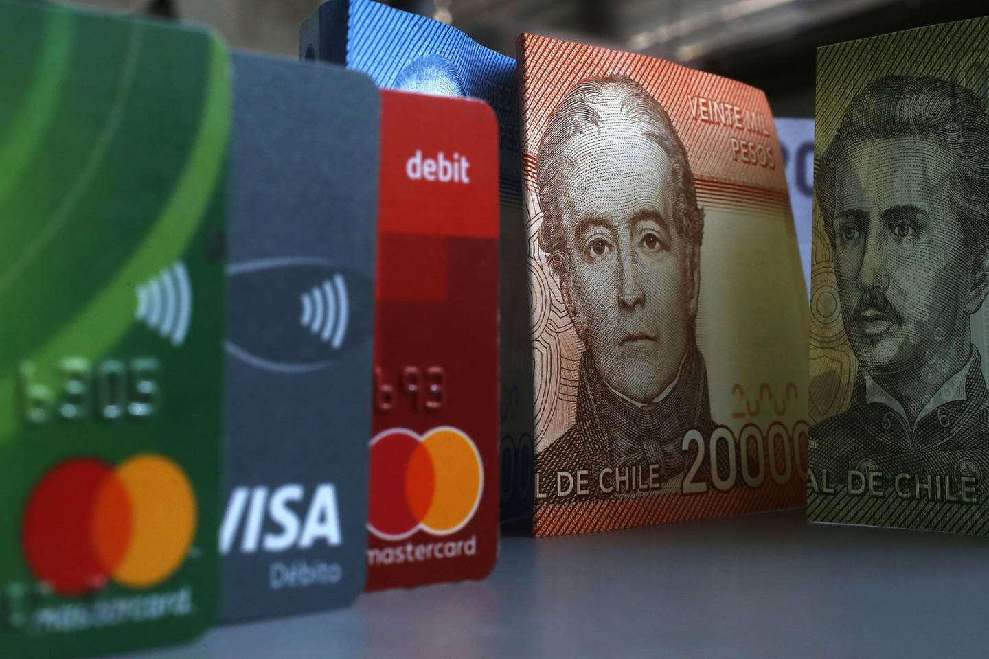 Billetes de diferentes montos y tarjetas de pago chilenas sobre una mesa.