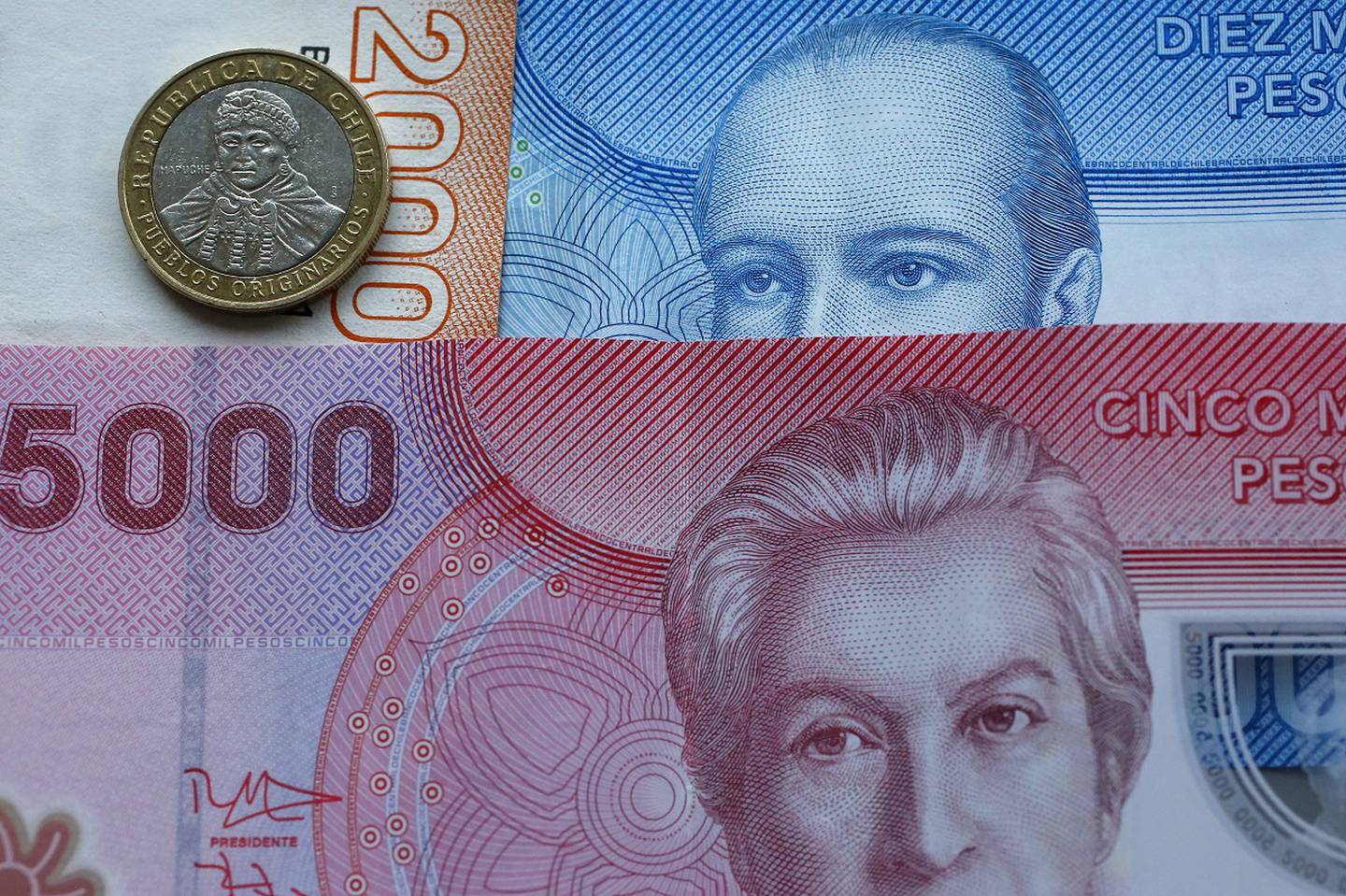 Billetes chilenos sobre una superficie con una moneda chilena de cien pesos.