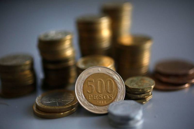 Pilas de monedas chilenas de distintas cantidades apiladas hacia arriba de fondo y delante una moneda de $500.