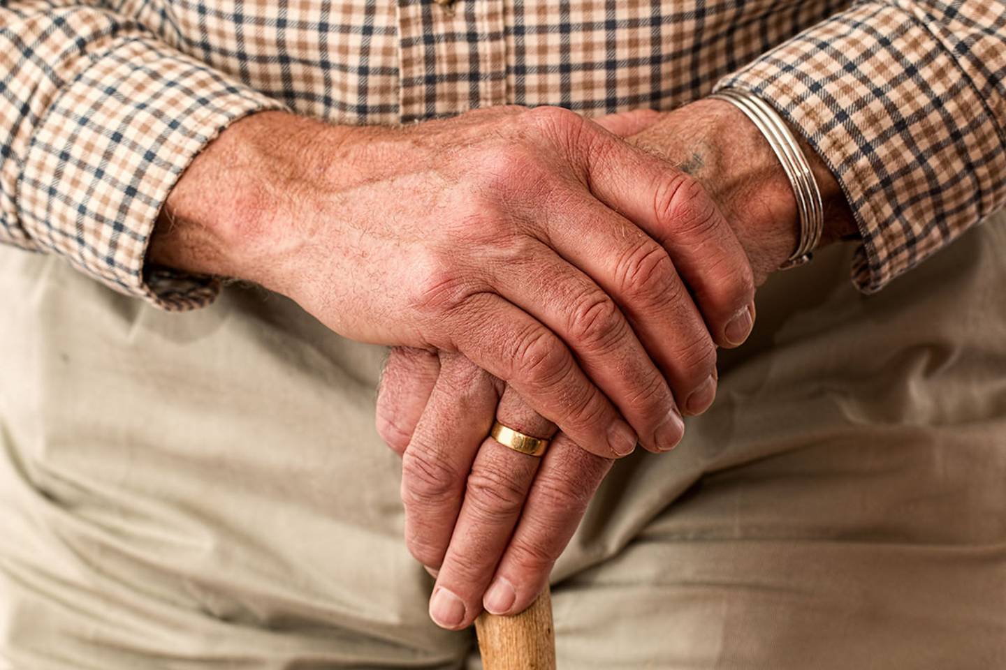 Adulto mayor cruza sus manos sobre un bastón.