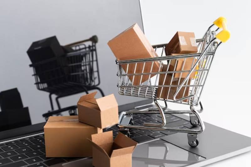 Carrito de compras con cajas encima de una computadora que hace alusión al e-commerce