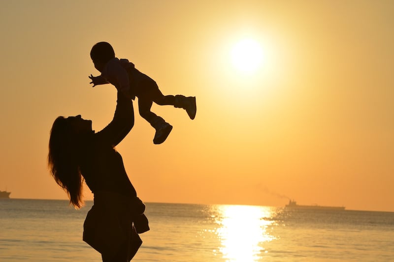 Una madre levantando a su hijo, en una puesta de sol.