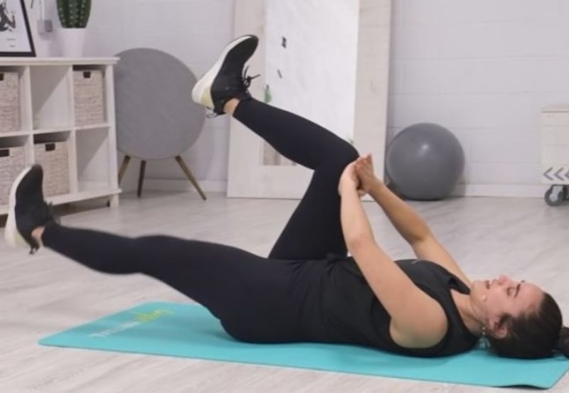 Mujer tendida en el suelo sobre un mat de yoga llevando sus rodillas al pecho.