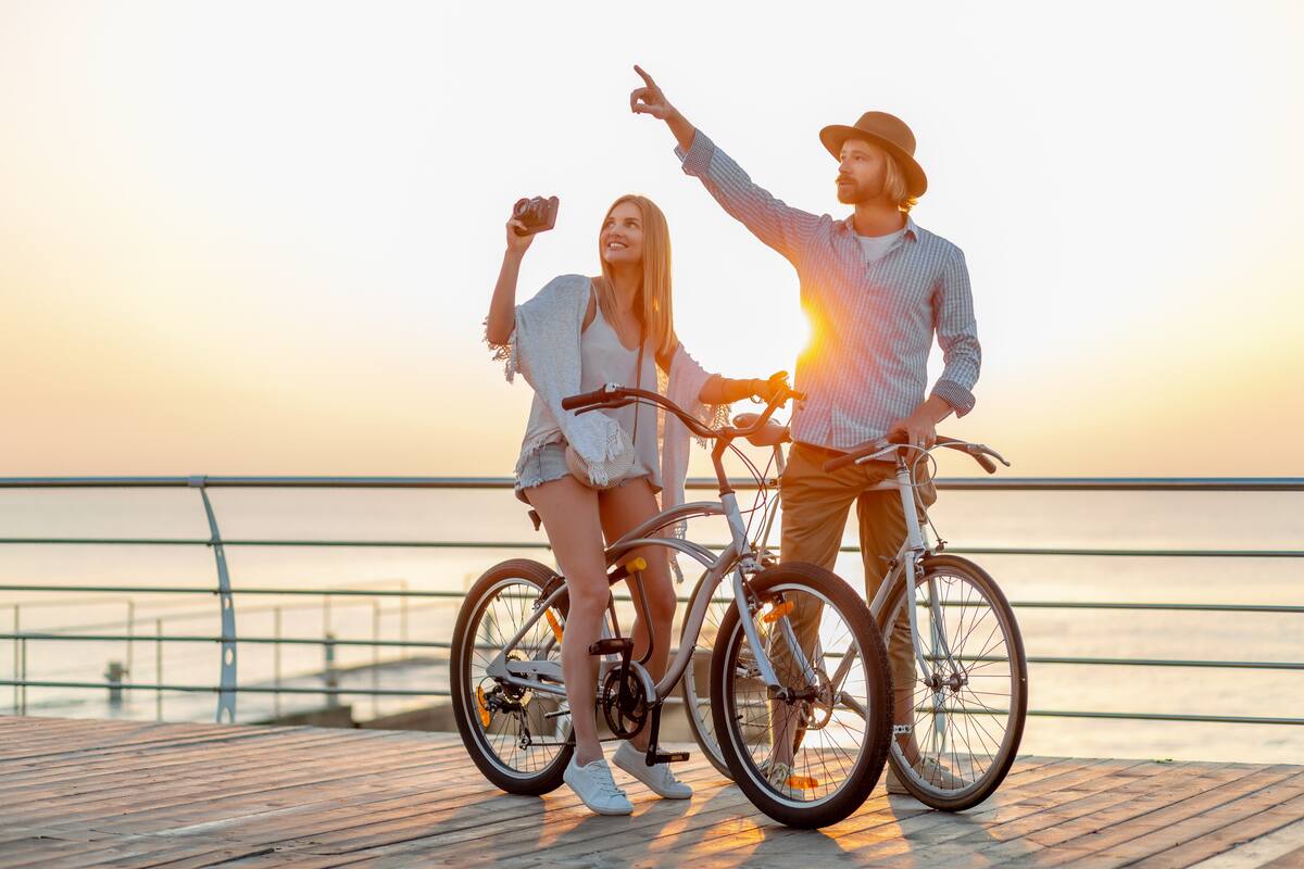 attractive happy couple traveling in summer on bicycles, man and woman with blond hair boho hipster style fashion having fun together, taking photos sightseeing