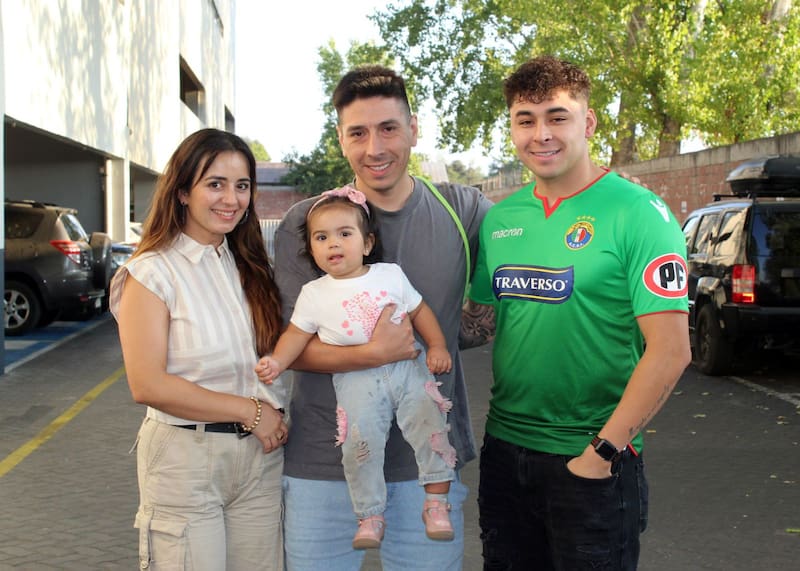 Hernán, el hijo menor del Clavo Godoy, sostiene a Leonor, su hija y la más pequeña de las nietas. A su lado, una nuera del entrenador y Emanuel, otro de sus trece nietos, vistiendo la camiseta de Audax. Foto: Pamela Juanita Cordero