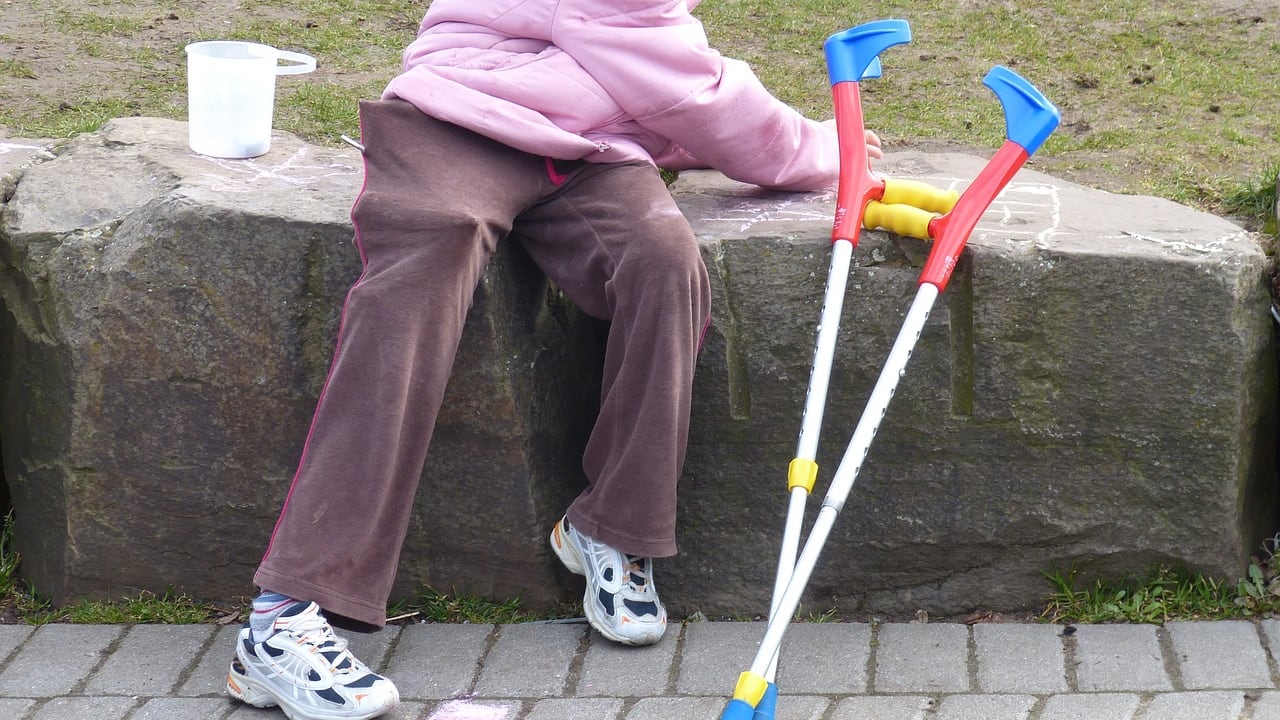 Piernas de una niña con sus muletas al costado sentada en una plaza en relación al subsidio de discapacidad.