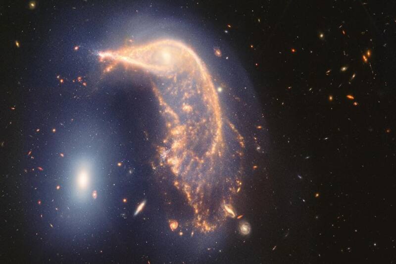 La galaxia espiral distorsionada del centro, el Pingüino, y la galaxia elíptica compacta de la izquierda, el Huevo, aparecen entrelazadas por una nube de gases y estrellas.