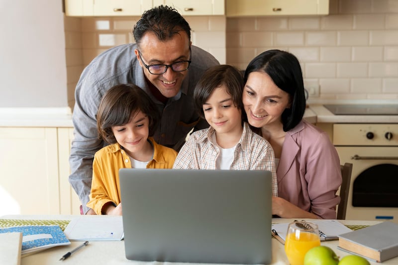Familia en su cocina viendo un computador, con cara de felicidad.