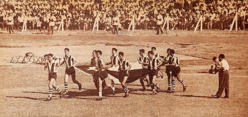 El elenco guaraní sale a la cancha del estadio de Puerto Sajonia de Asunción portando la bandera chilena. Eran otros tiempos. Foto: revista Estadio.
