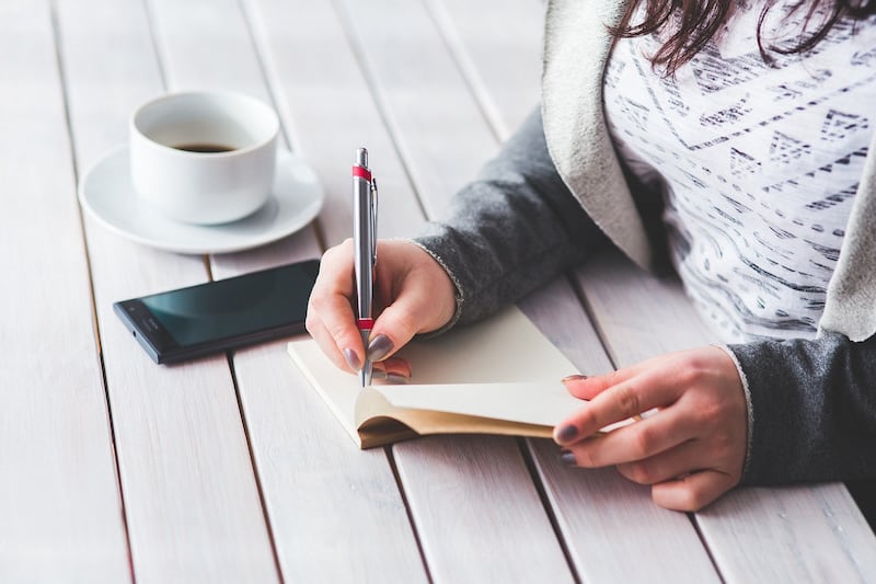 Manos de una mujer escribiendo sobre una mesa y una tasa de café.
