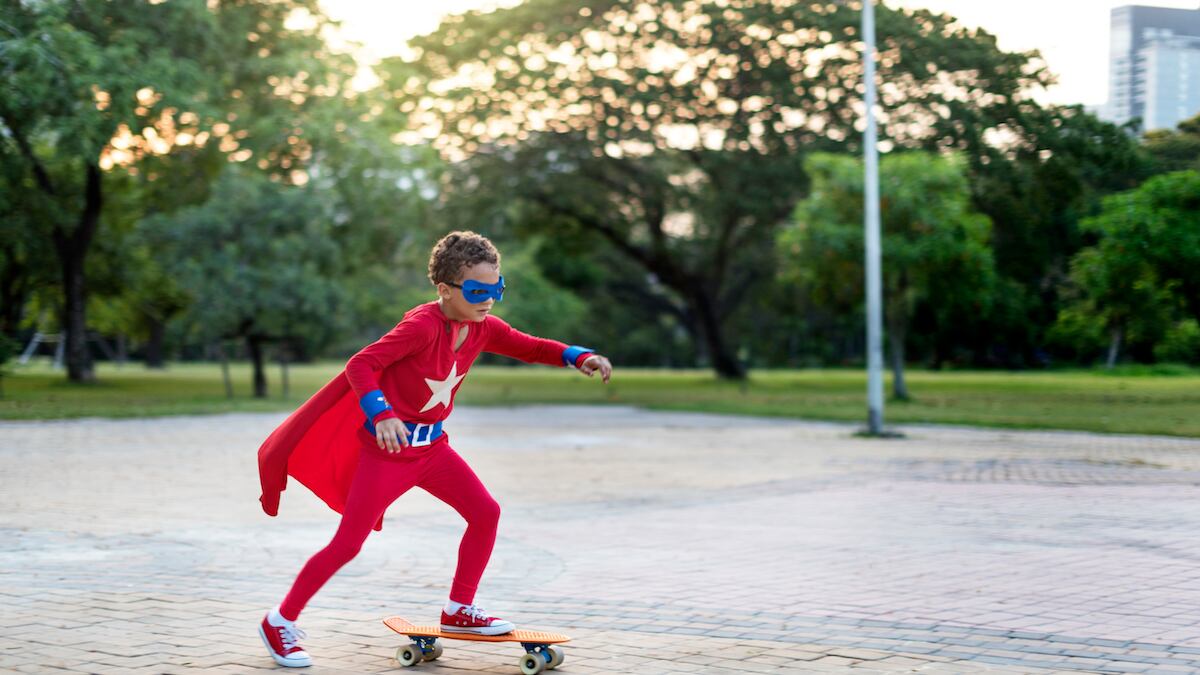 niño vestido de superhéroe, andando en patineta en un parque.