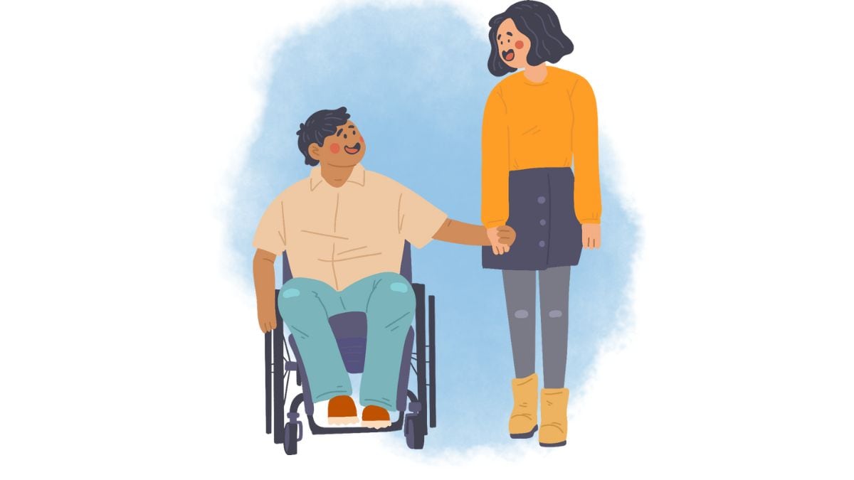 Persona con discapacidad en una silla de ruedas tomando de la mano a otra persona parada junto a él mientras ambos sonríen.