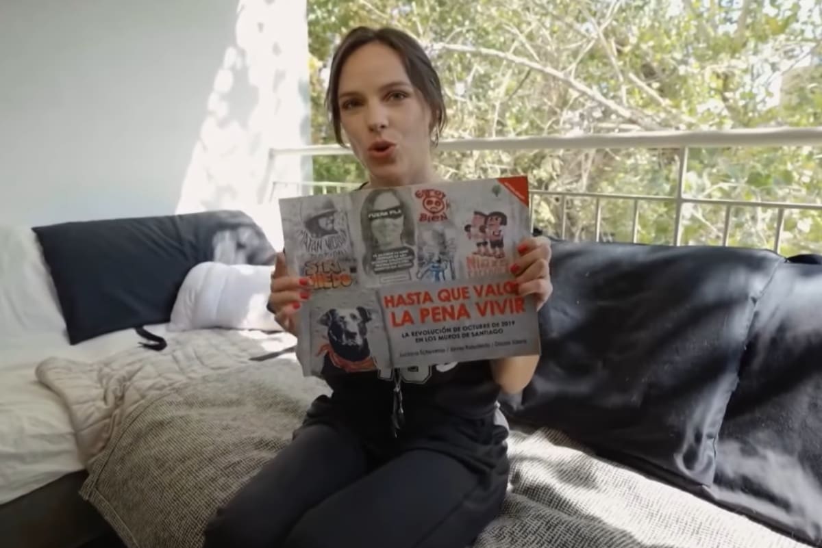 mostrando el libro de su autoría sobre el Estallido Social. Créditos: La Divina Comida.