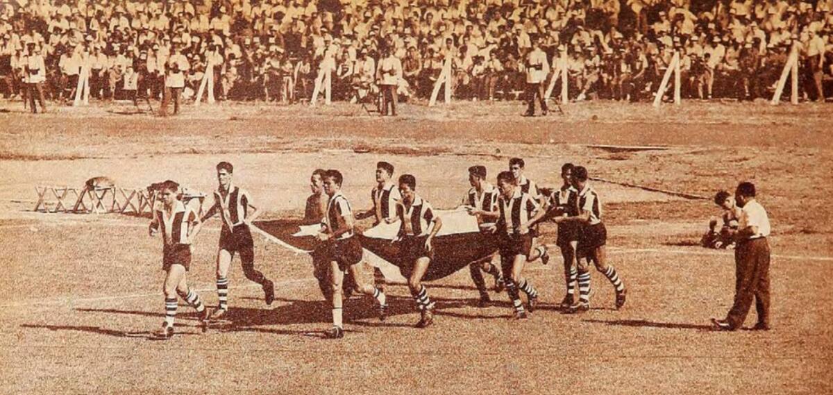 El elenco guaraní sale a la cancha del estadio de Puerto Sajonia de Asunción portando la bandera chilena. Eran otros tiempos. Foto: revista Estadio.